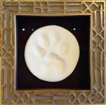 Plaster of paris cast of dog's paw print in gold frame.