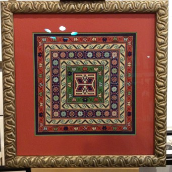 Photo of colorful needlework in geometric patterns that has been framed with an orange matte and carved gold frame.