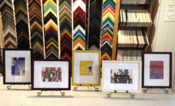 Five framed postcards lined up on framer's counter.