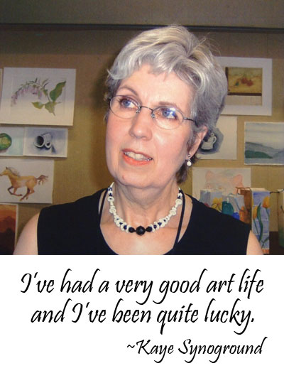 Photo of Kaye Synoground standing in front of some of her art work. Below is a quote from Kaye: "I've had a very good art life and I've been quite lucky."