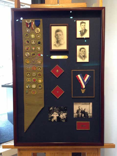 Shadow box full of scouting medals and old black and white pictures.