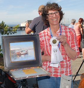 Susan Kuznitsky holding up one of her paintings and a ribbon it won in an art show