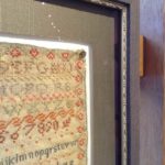 Close up of antique sampler framed behind glass.