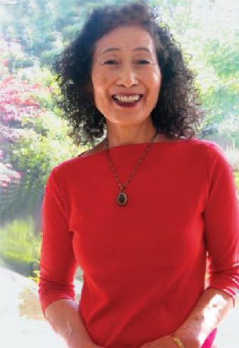 Noriko Hirayama, smiling broadly, standing in front of colorful trees.